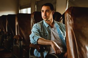 Country artist Jordan Shaw sits thoughtfully in a train car with vintage brown leather seats and warm natural lighting.