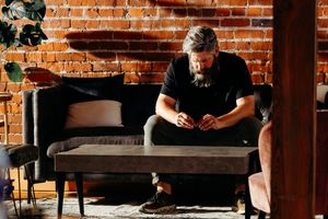 A person in black clothing sits on a gray couch against a exposed brick wall at a video shoot for Cross Point Church.