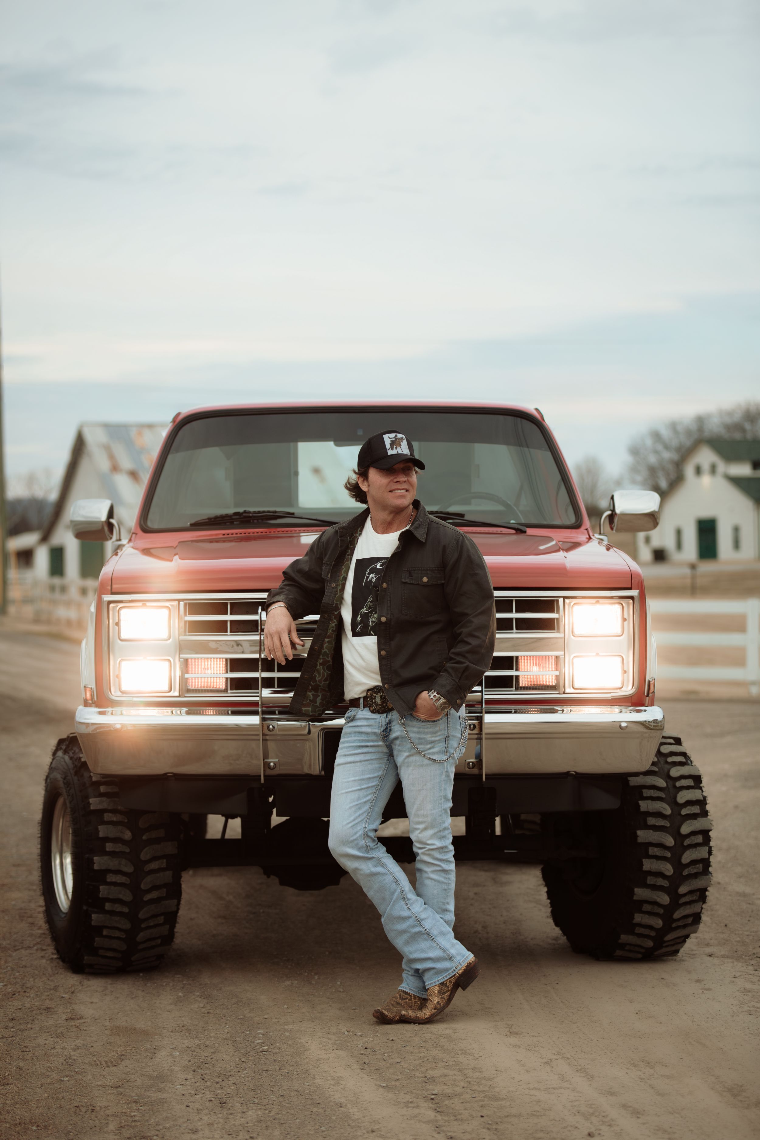 A vintage red pickup truck with large off-road tires is displayed in a series of dramatic shots at sunset.