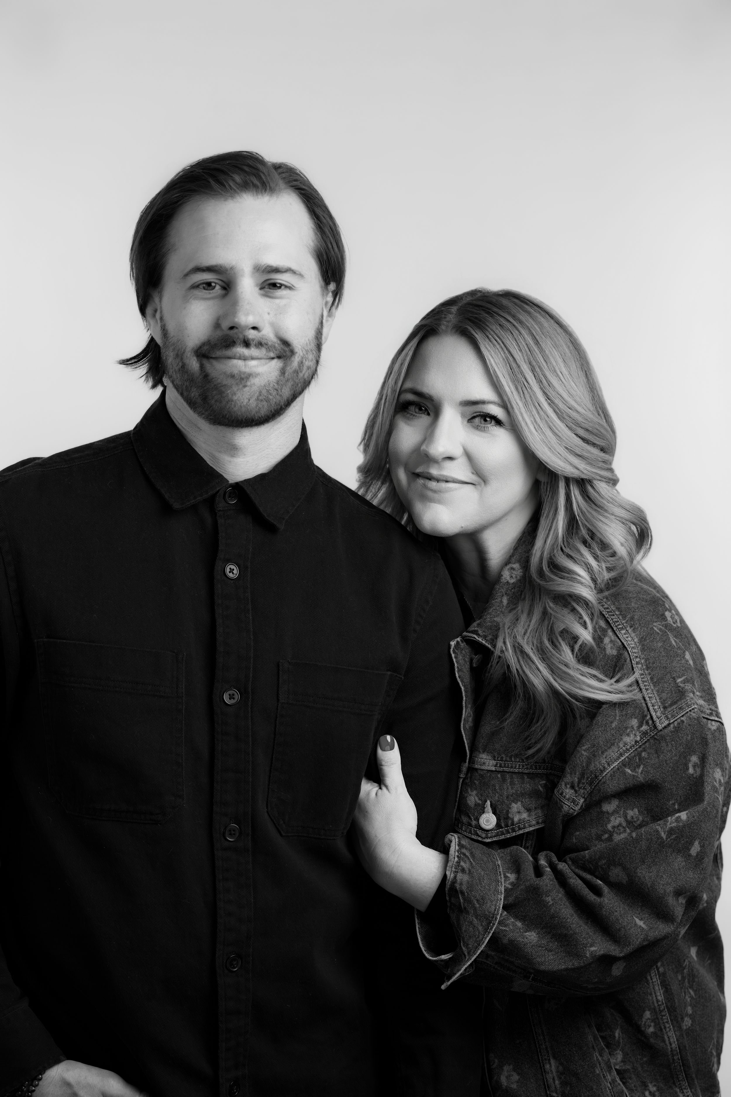 Black and white portrait of a couple posing together, with him in a dark shirt and her wearing a denim jacket.