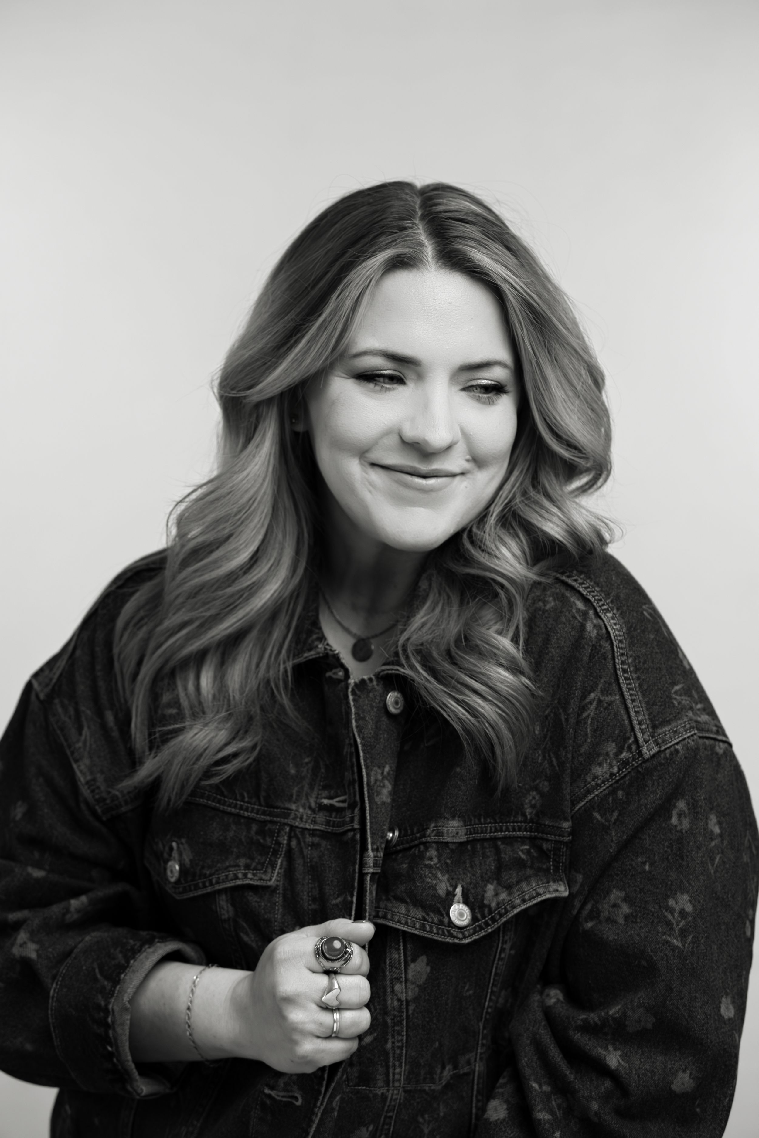 Black and white portrait of someone smiling while wearing a denim jacket and styled wavy hair.