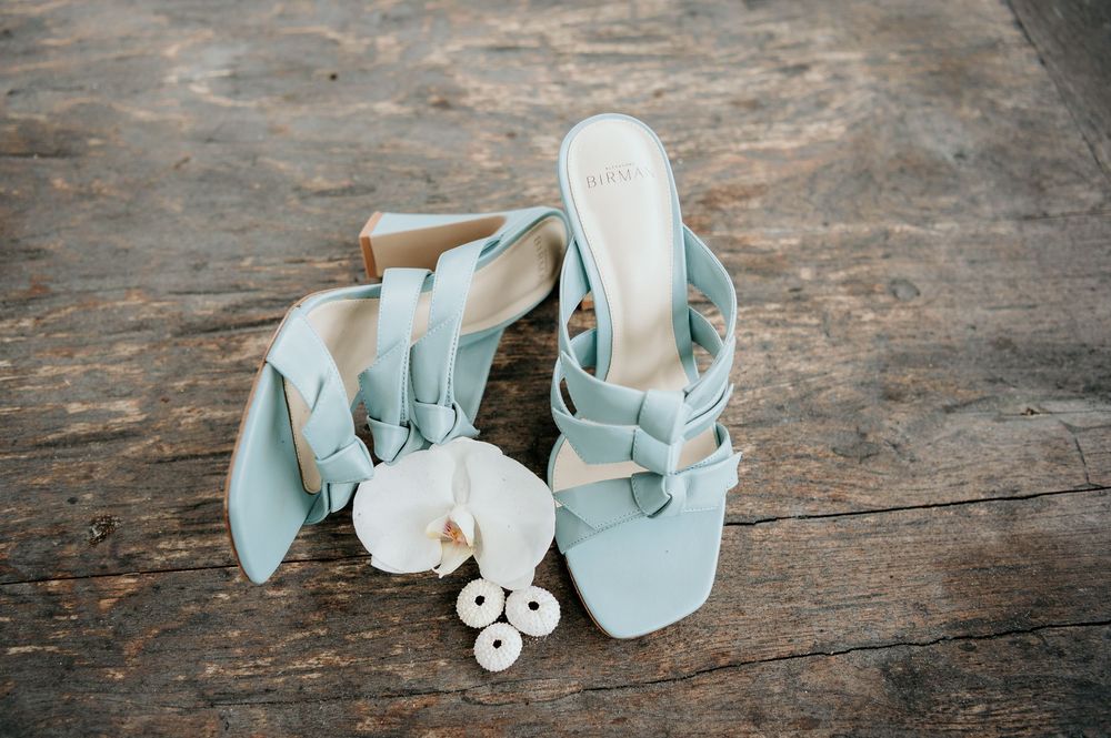 Light blue bridal sandals with pearl accessories arranged on rustic wooden floor.
