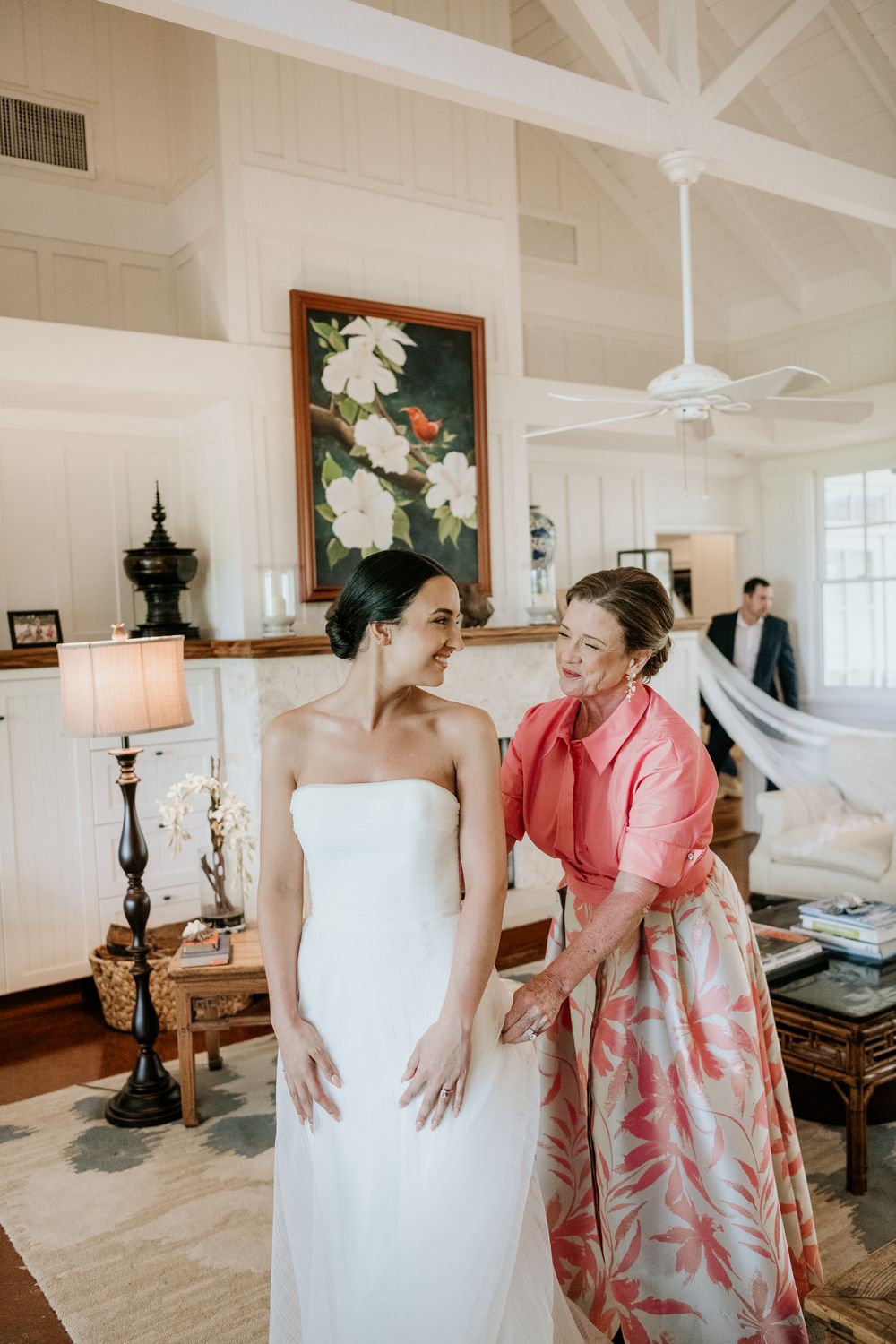 Two women share an intimate moment in a bridal suite with white vaulted ceilings and floral artwork on the wall.