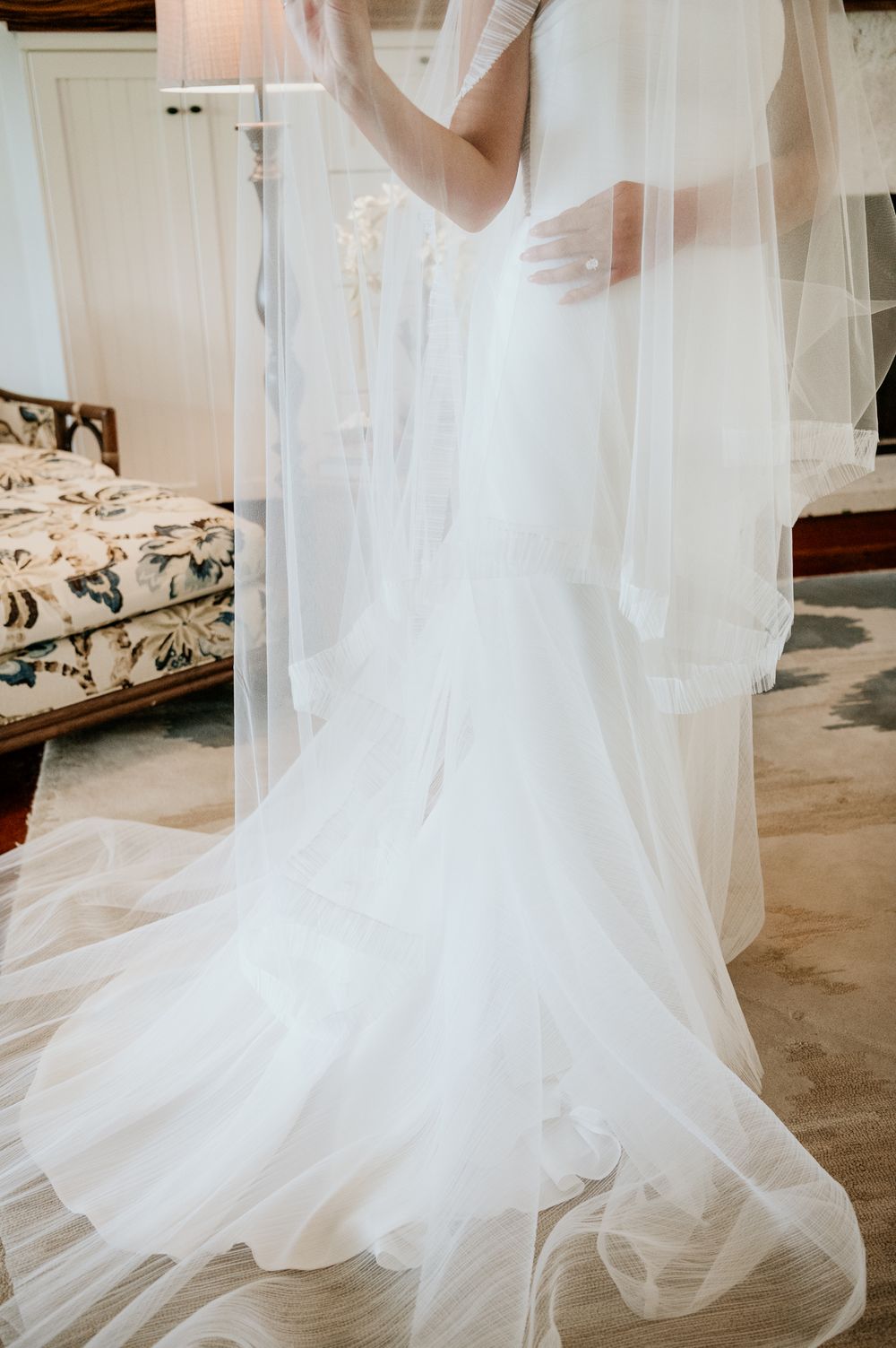 Elegant white wedding dress with flowing tulle veil and mermaid silhouette photographed in soft natural light.