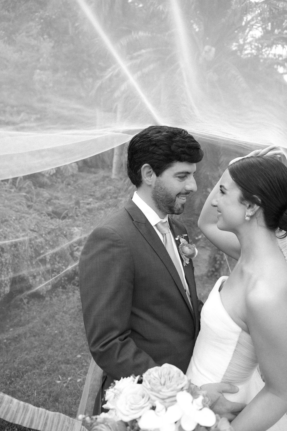Black and white wedding photo showing a tender moment between newlyweds under a flowing veil.