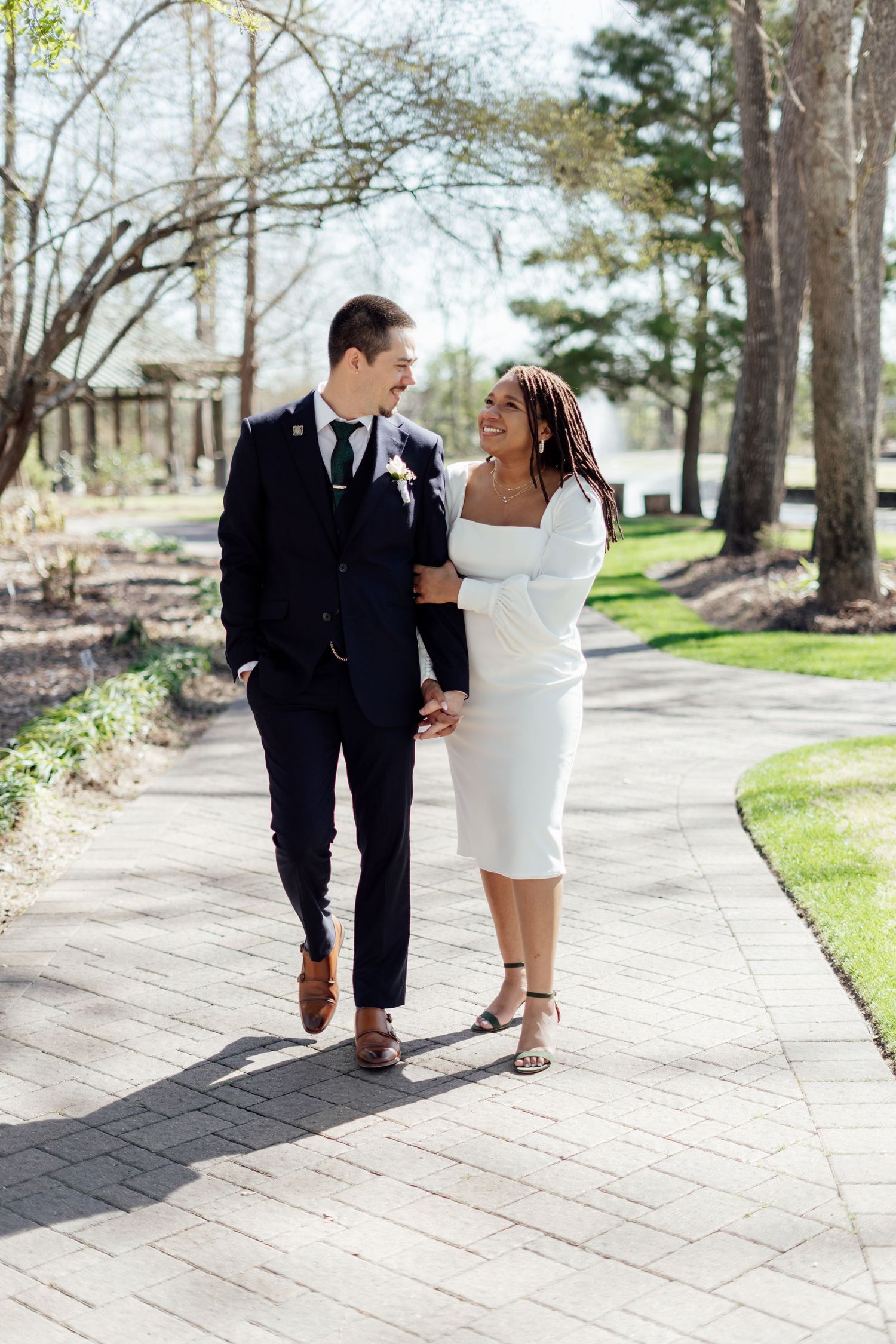 A romantic wedding couple shares a kiss outdoors while holding a white bouquet in a natural setting.