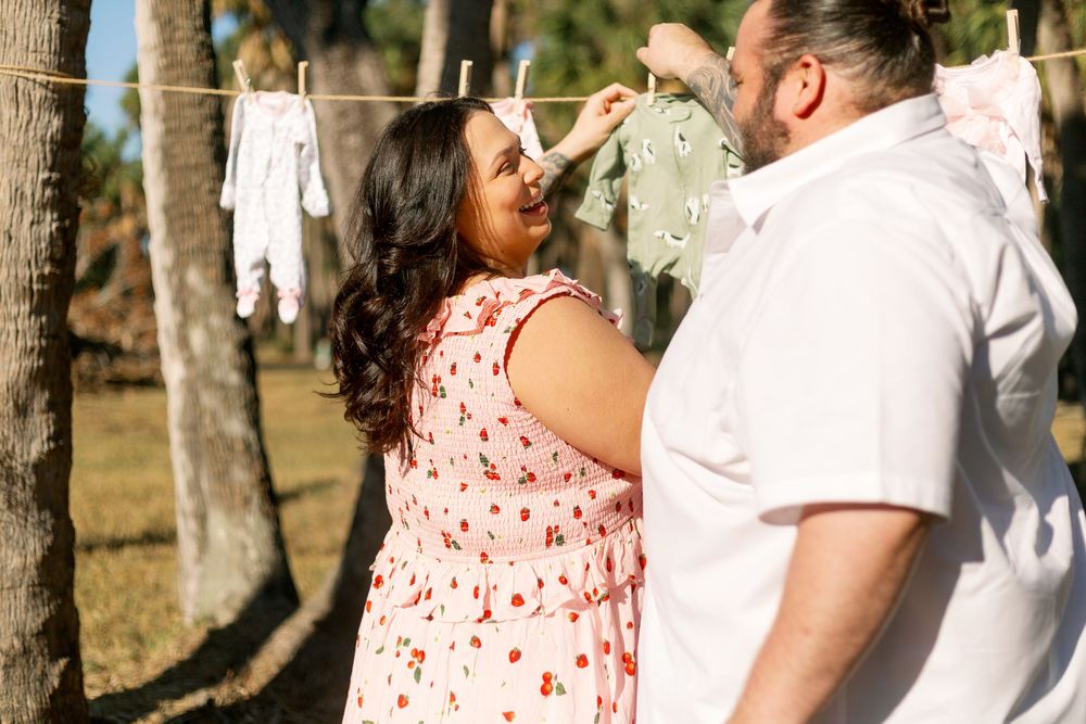 A couple shares a playful moment outdoors with clothesline and palm trees in the background.