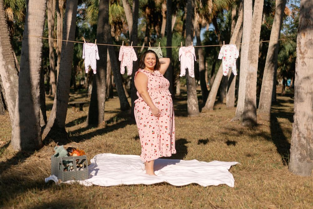 A polka dot dress-clad figure stands by a clothesline with baby clothes hanging between trees in a wooded area.