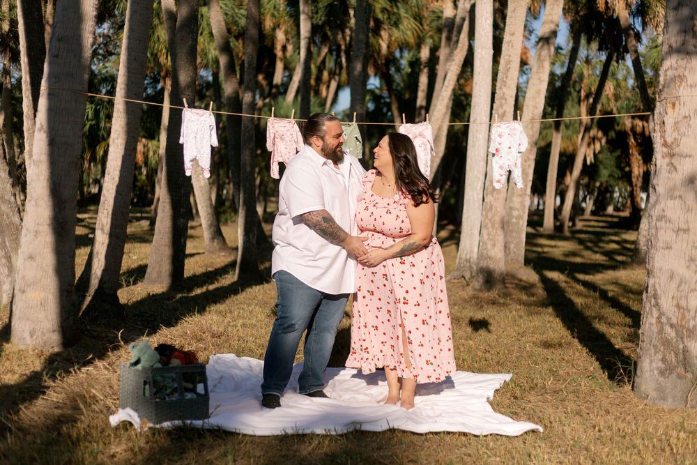 A couple shares a romantic moment on a picnic blanket surrounded by palm trees in a sun-dappled grove.