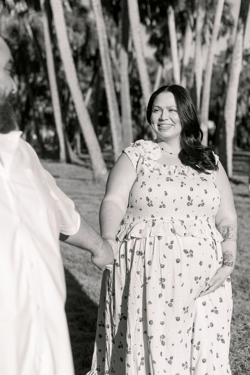A person in a floral print dress smiles while standing outdoors among eucalyptus trees in a black and white photo.