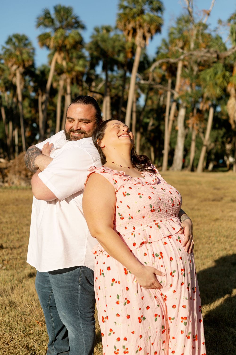 A couple shares a tender moment outdoors with palm trees in the background during golden hour.