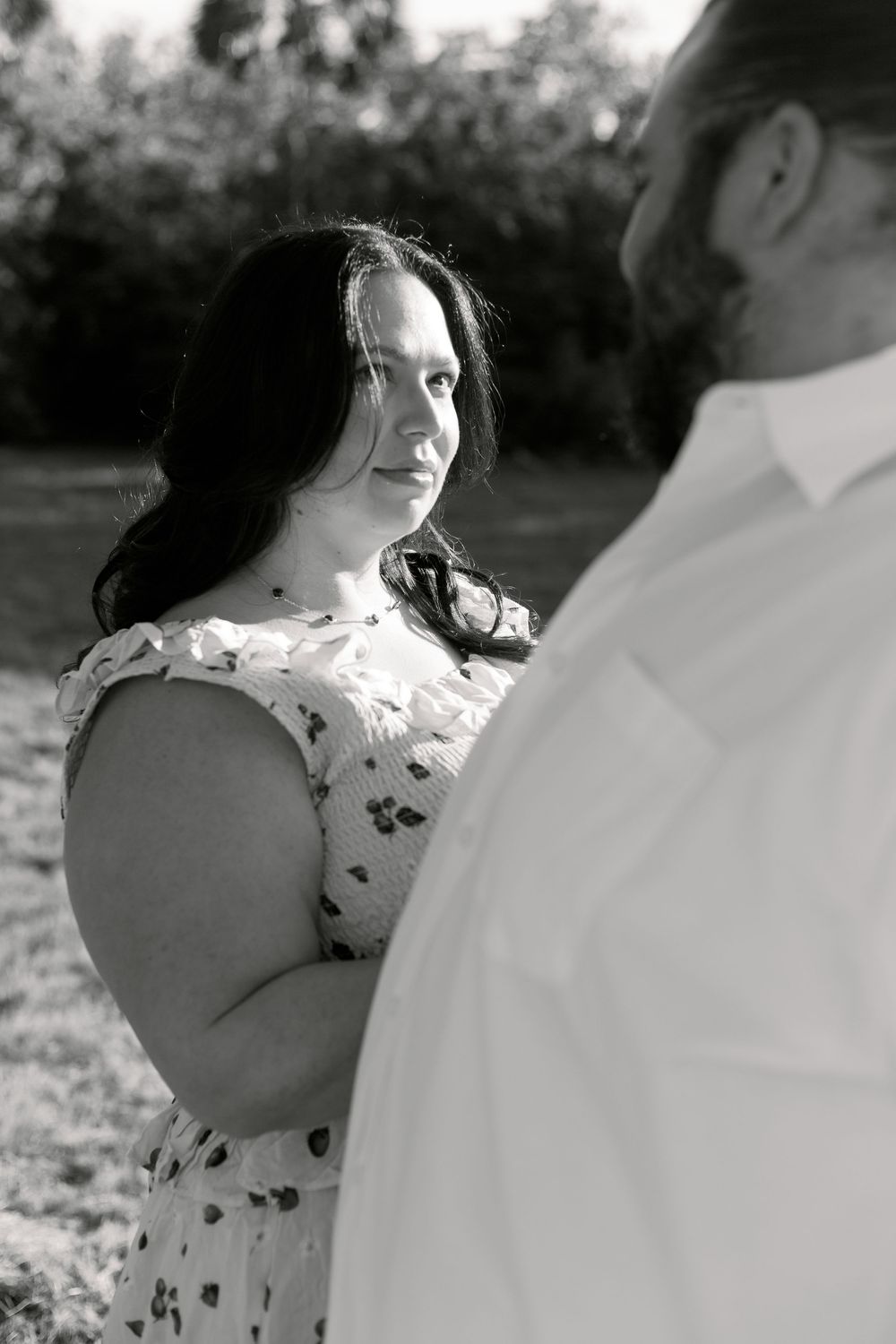 Black and white photo showing a couple during an intimate moment outdoors, with person wearing a floral dress in focus.