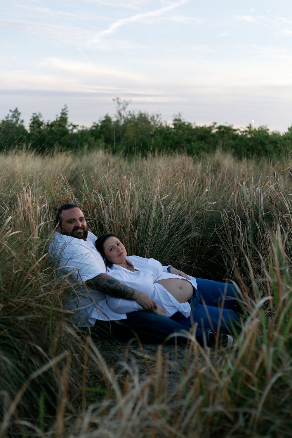 A couple relaxes together in tall grass during sunset, lying back in a peaceful meadow.