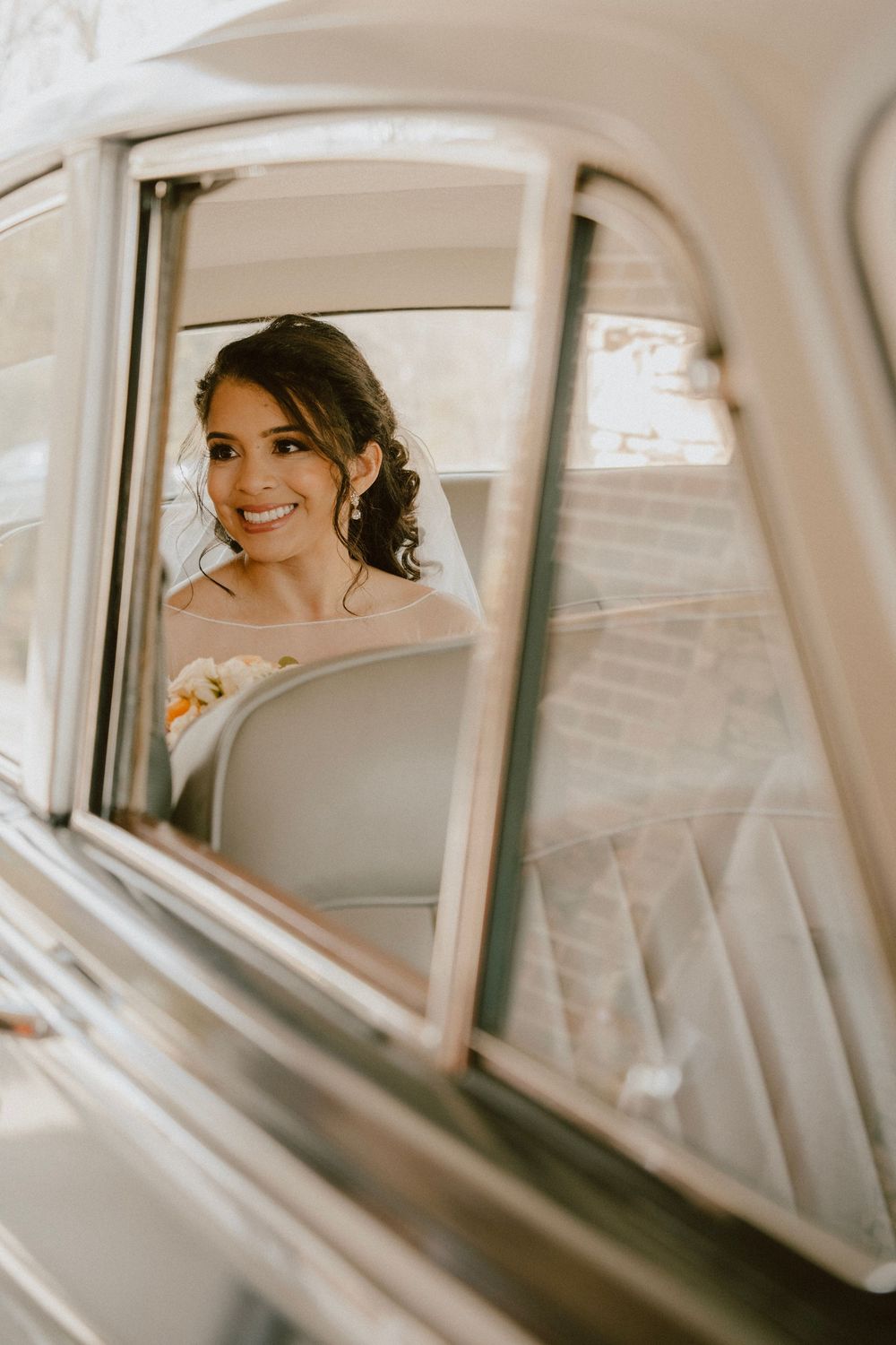 Reflection of a bride in vintage car window showing joyful expression.