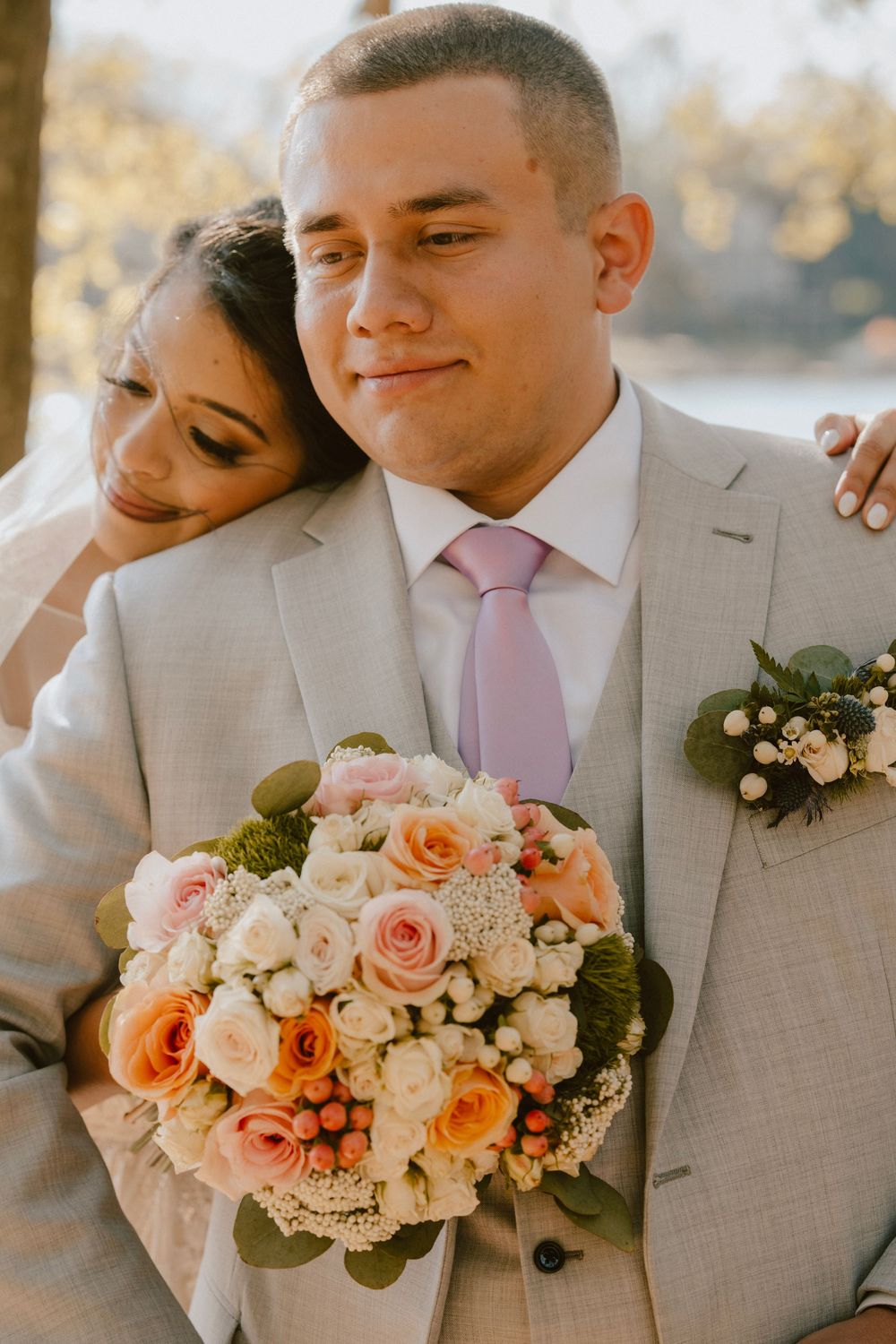 Couple poses with peach and cream wedding bouquet during outdoor photo session.