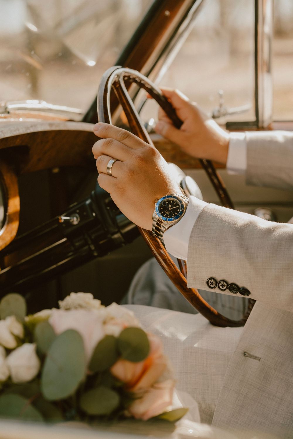 Close-up of hands on vintage car steering wheel showing wedding ring and luxury watch.