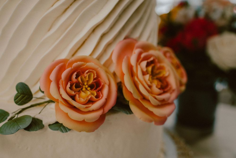 Macro shot of peach-colored roses with green foliage decorating a wedding cake.