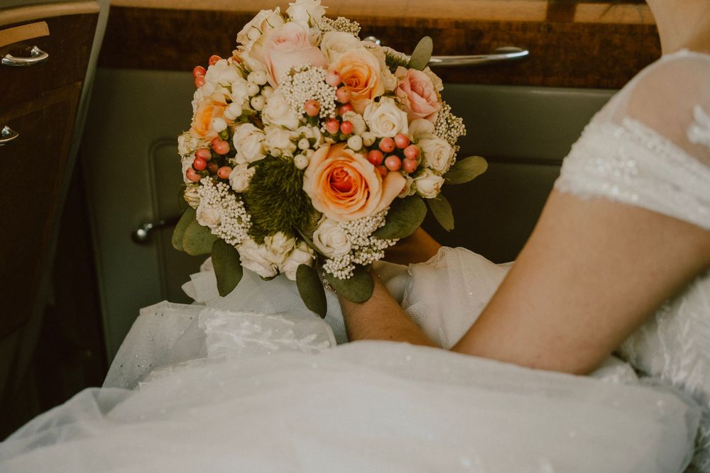 A delicate peach and white wedding bouquet rests on a bride's lap.