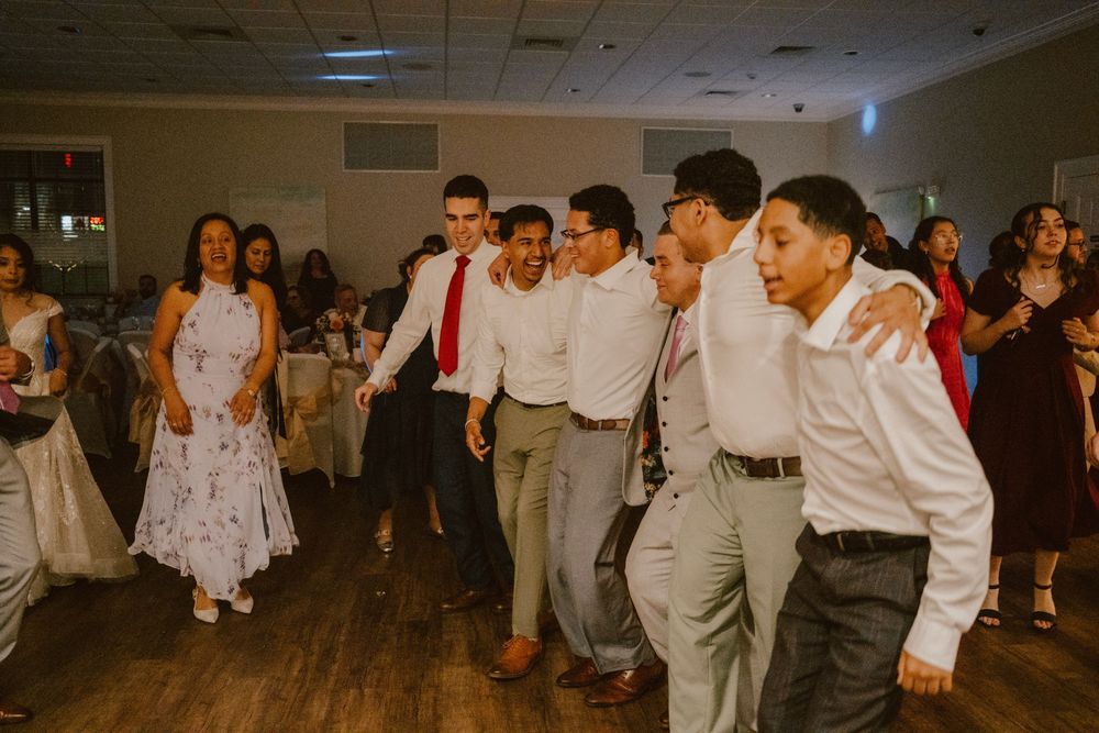 Wedding guests dancing and celebrating on a wooden dance floor at a reception.