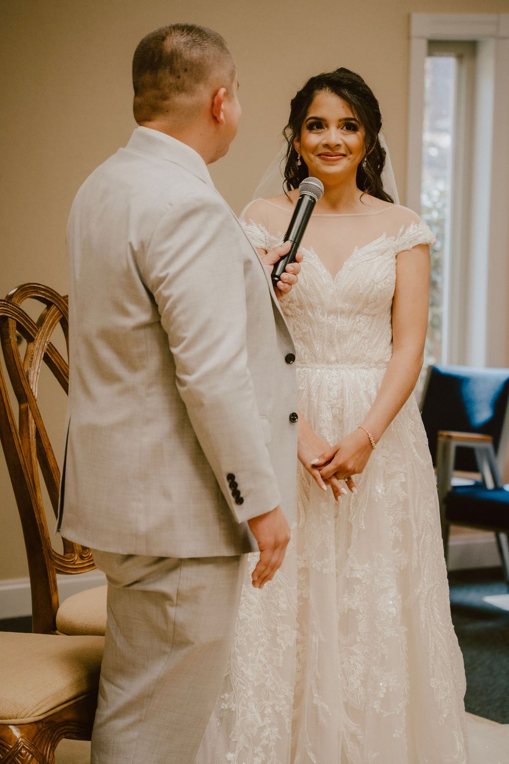 A couple exchanges vows during an indoor wedding ceremony with the groom holding a microphone.