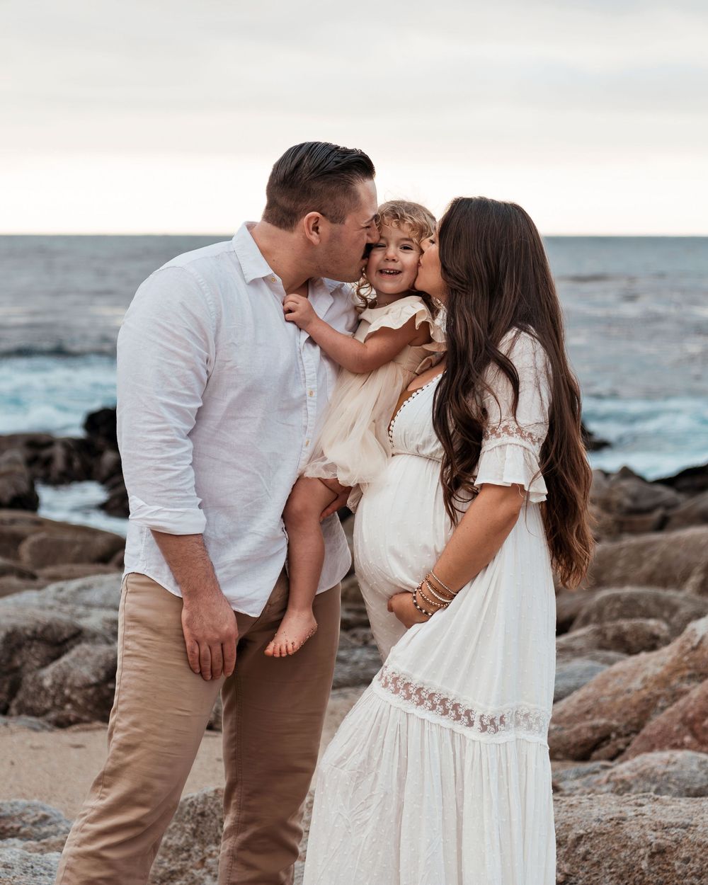 Family sharing tender moments together on rocky coastal shore.