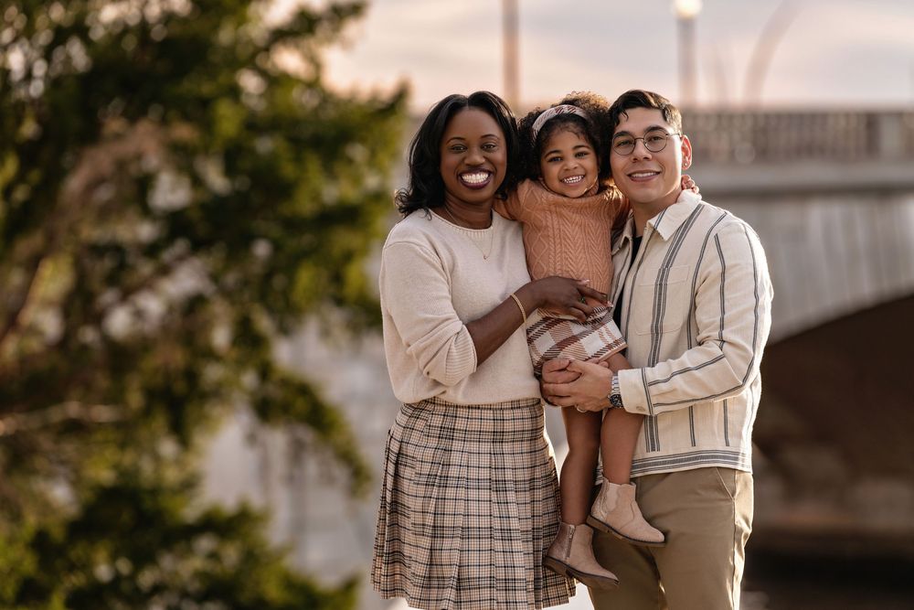 A group of people embrace and laugh together outdoors during a family photo session at sunset.