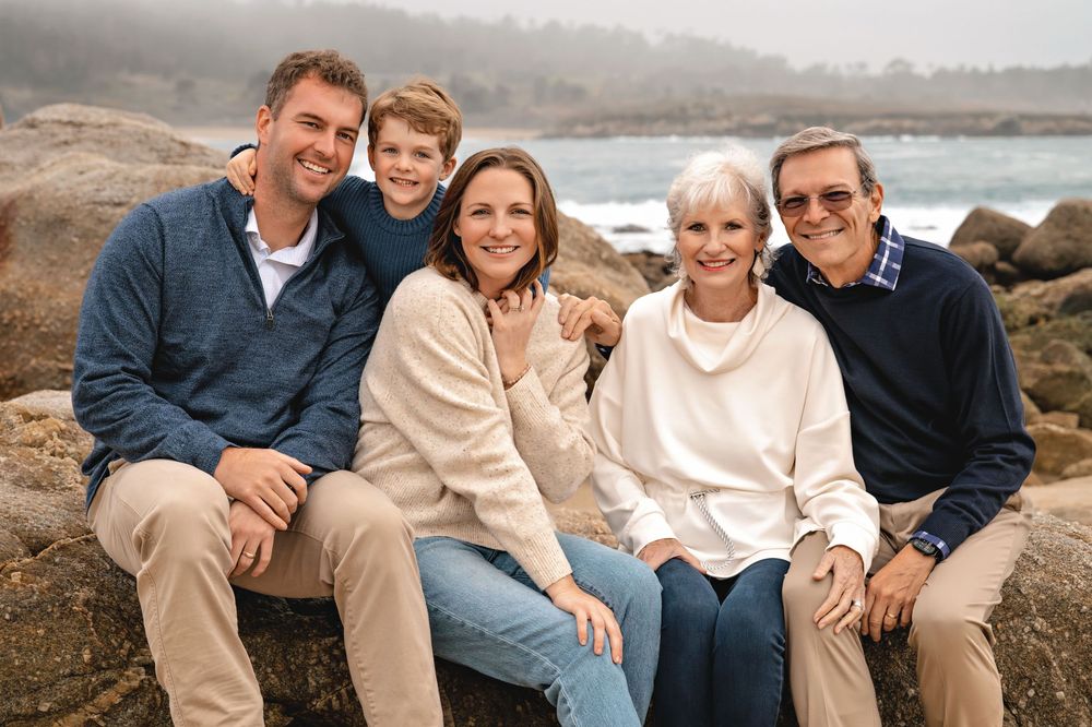 A casual group wearing coordinating cream and blue outfits poses together on a rocky coastal beach.