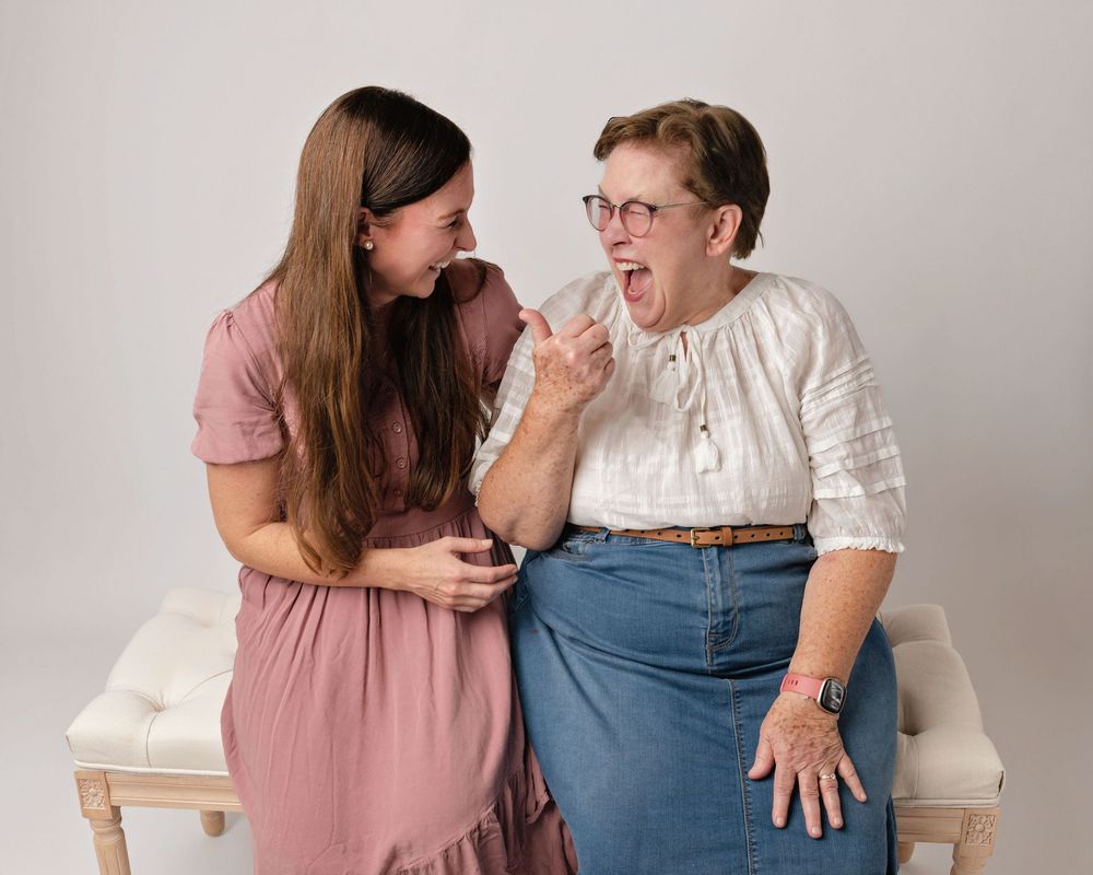 Two people sharing joyful laughter while sitting on white bench.