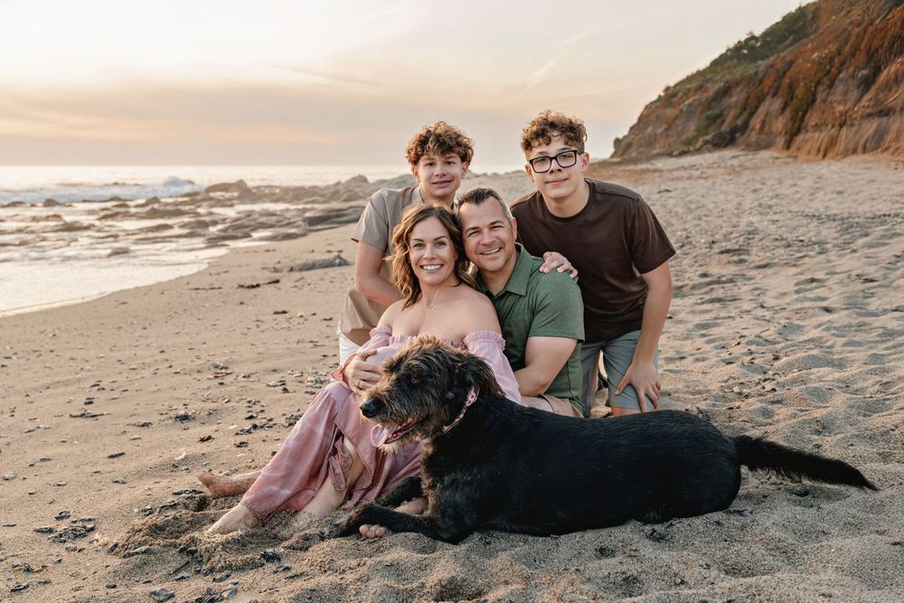 Family and dog sitting together on a sandy beach at sunset while enjoying quality time together.