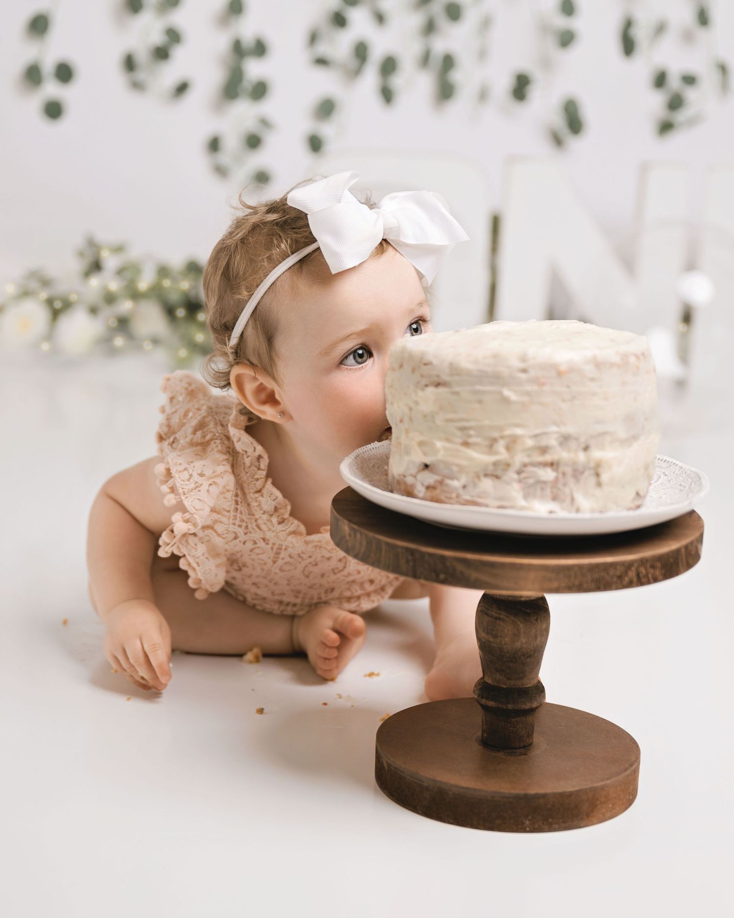 Baby reaching for white frosted cake during first birthday cake smash photo session.