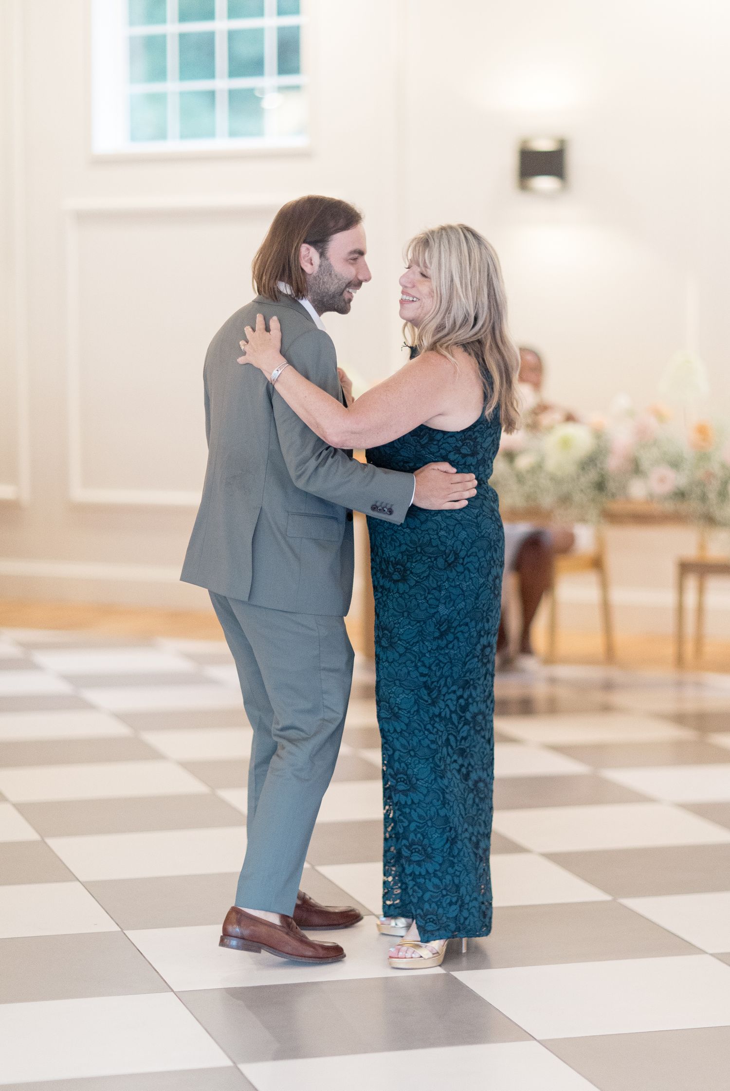 A couple in formal attire dancing together on a checkered floor in an elegant bright interior space.