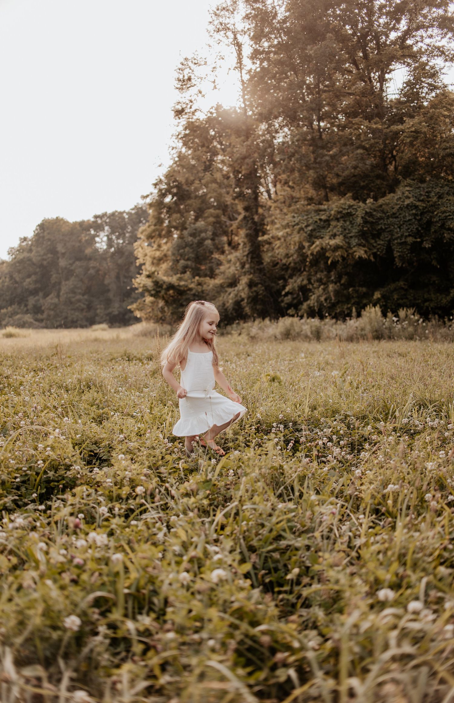 A person in a white dress twirling in a sunlit meadow during golden hour.