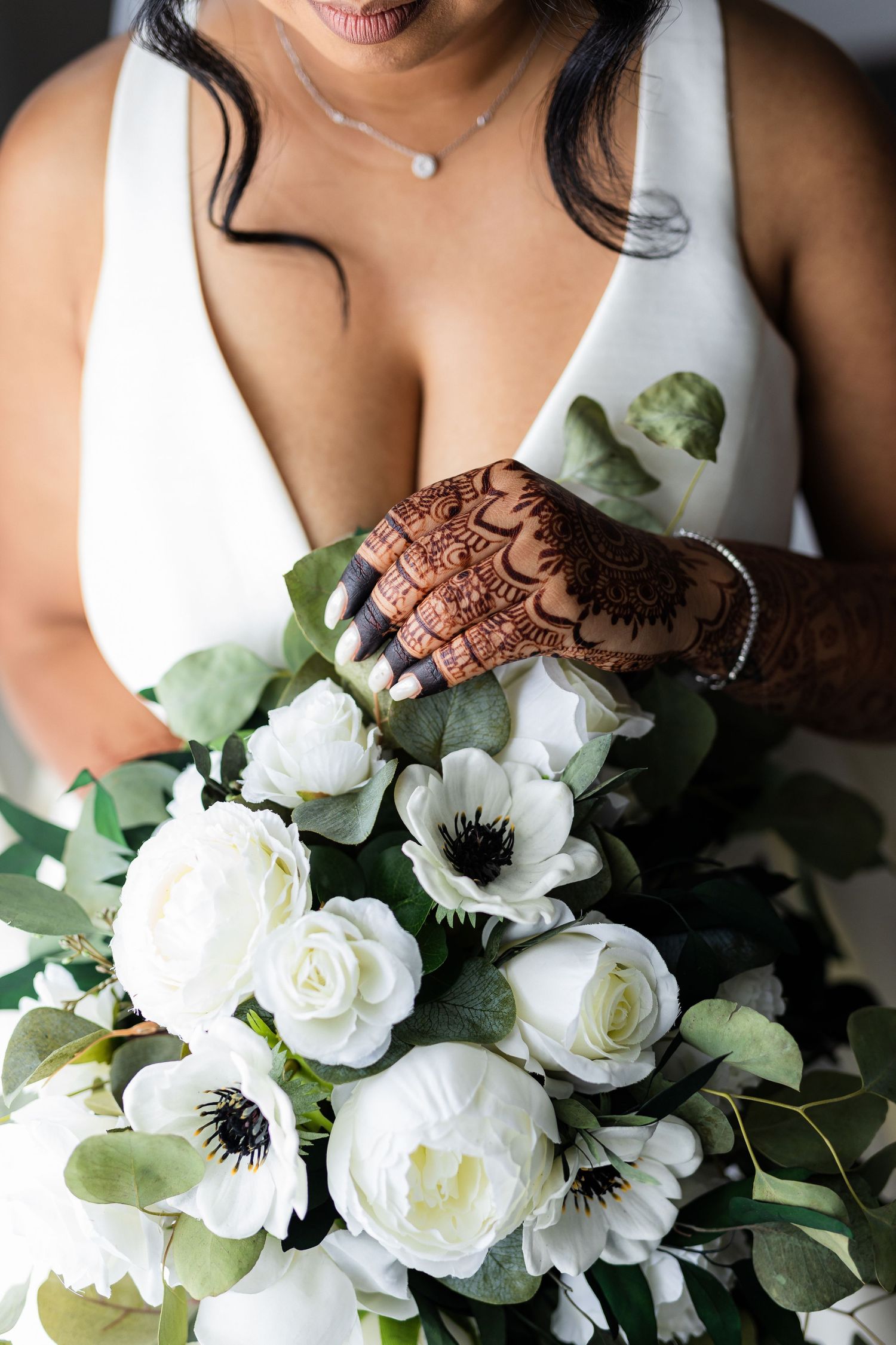 Elegant white bridal bouquet with roses and anemones held by hands with henna designs.