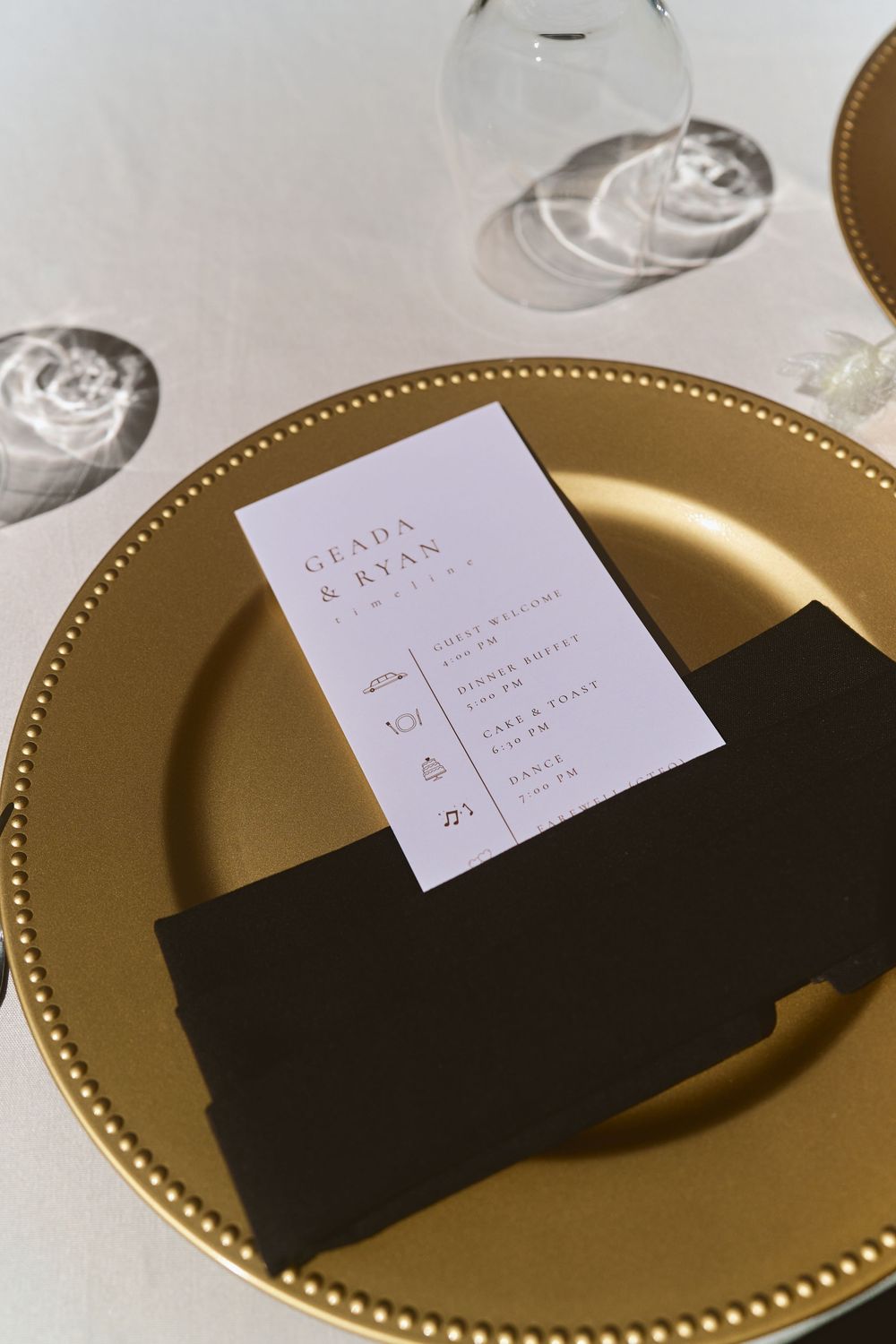 Elegant wedding place setting with gold charger plate, black napkin, and white menu card for Geada and Ryan.