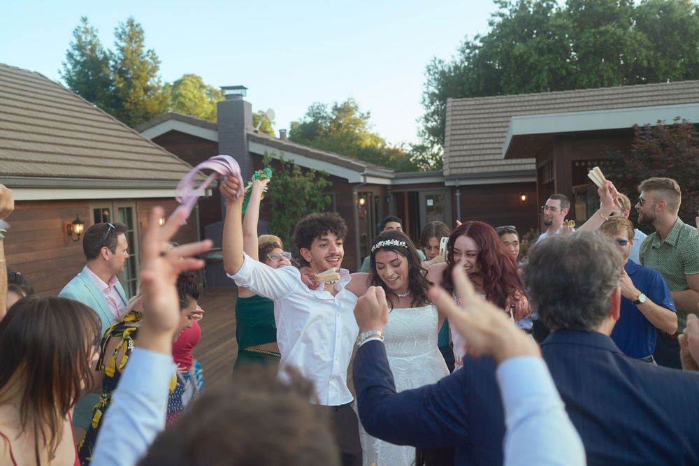 Wedding photography image of a bride and groom celebrating joyfully with wedding guests during an outdoor reception dance.