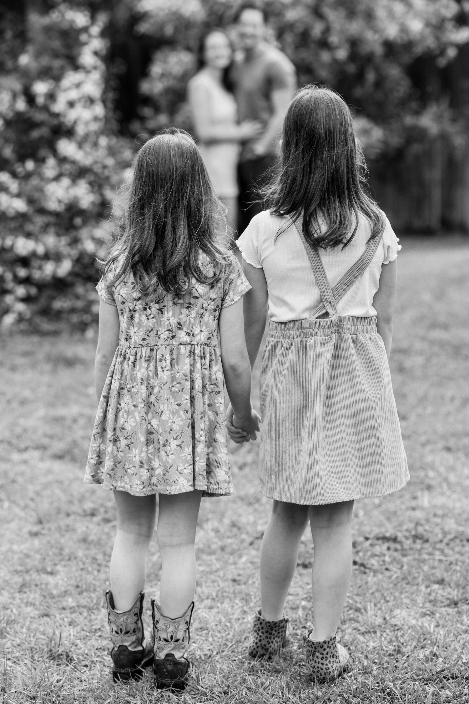 Two girls holding hands looking at their parents in the distance.