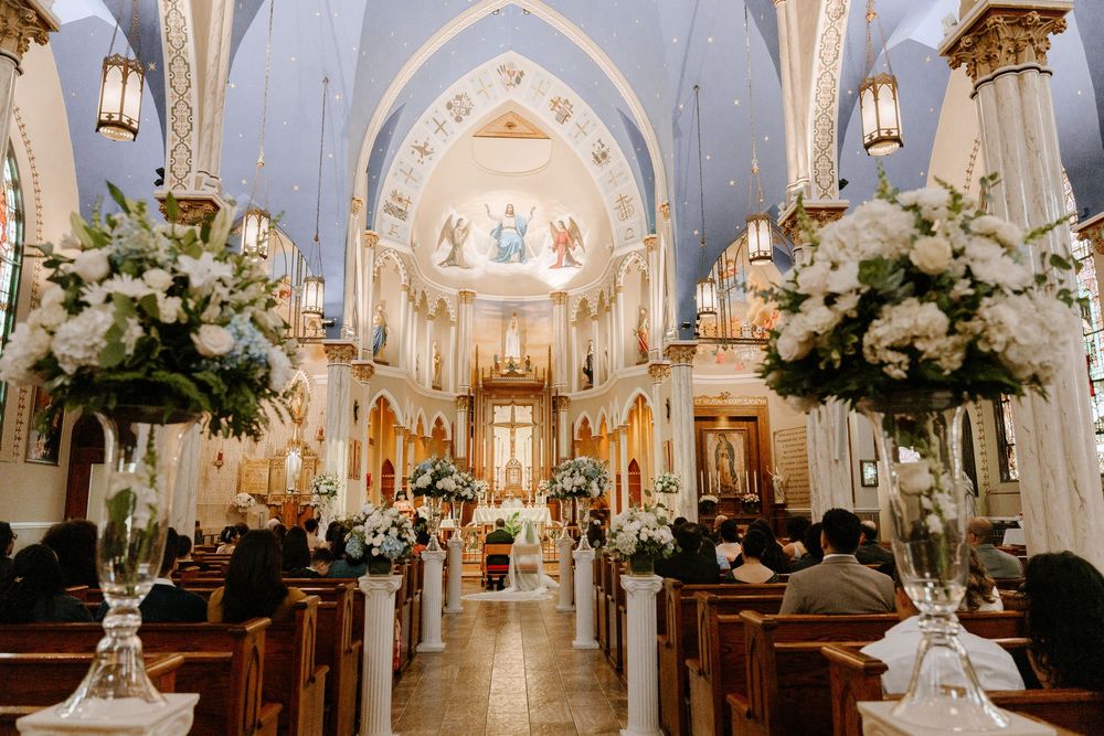 Interior of an ornate Catholic church decorated with white floral arrangements for a wedding ceremony.