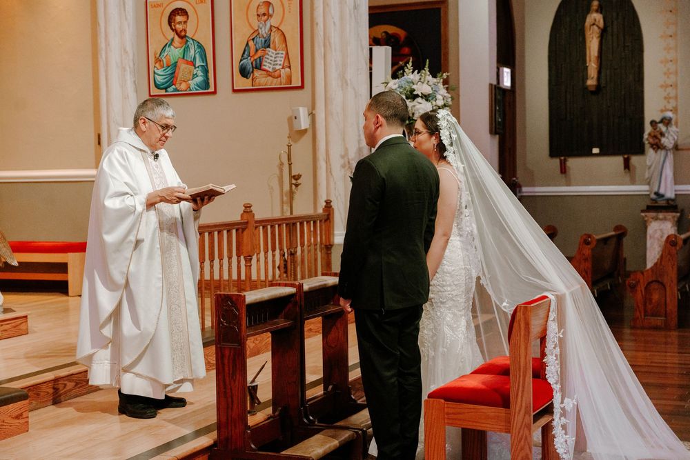 A wedding ceremony taking place in a Catholic church with altar, pews and traditional wedding attire.