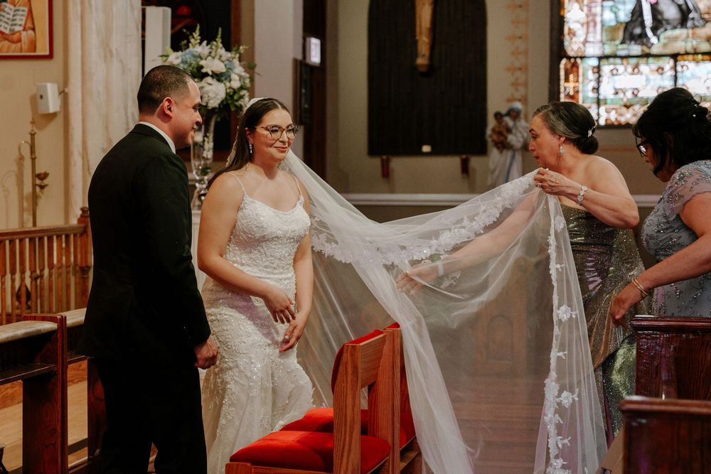Bride in white gown with flowing veil getting ready in church sanctuary before wedding ceremony.