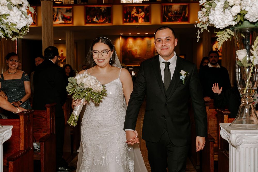 Wedding party enters grand reception venue with glittering chandeliers and elegant white floral arrangements.