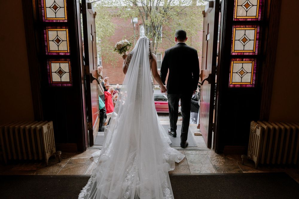 Dramatic silhouette of a wedding couple walking through a church doorway with stained glass windows.