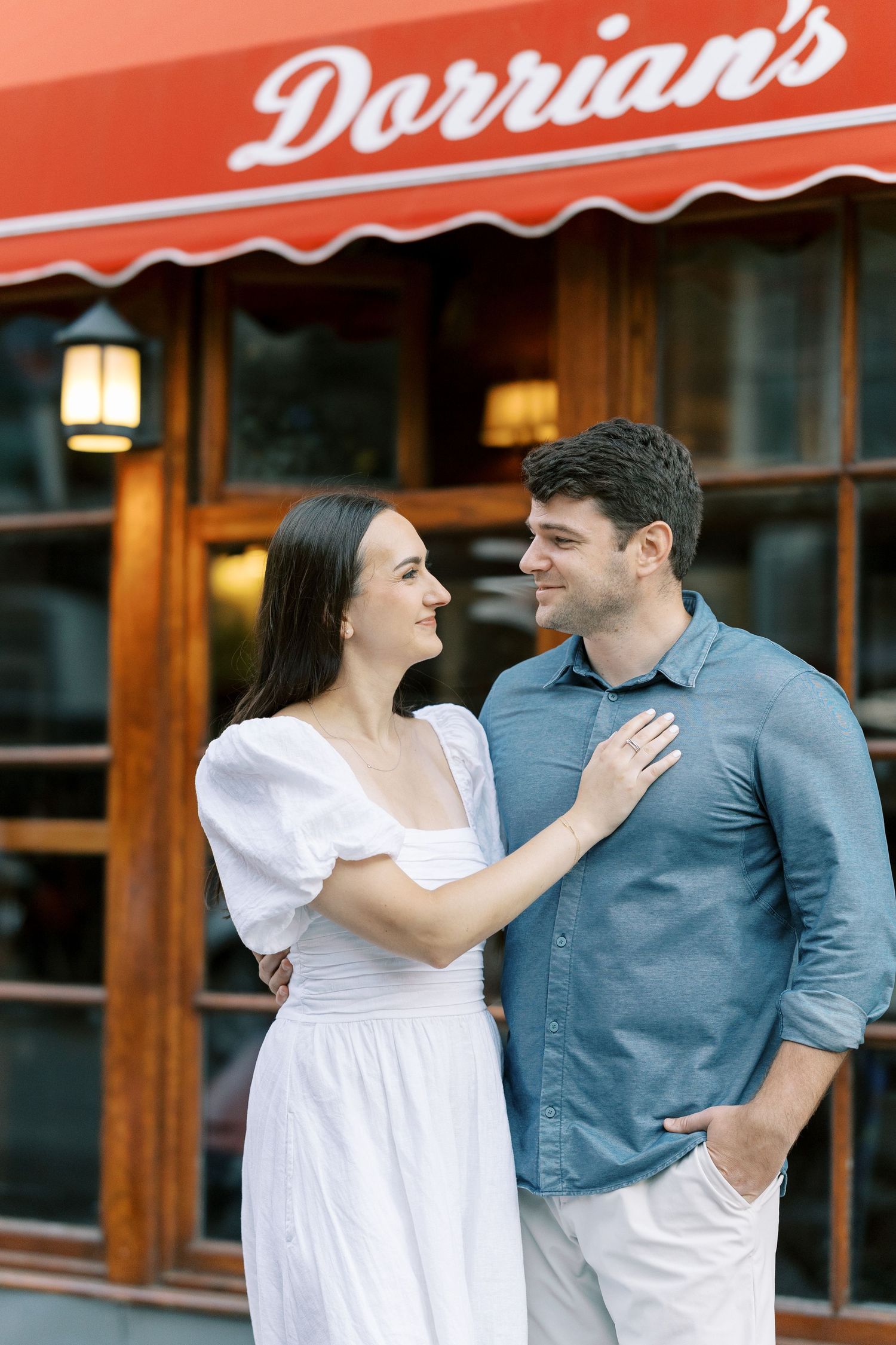 A couple shares laughter and flirtatious moments in front of a restaurant establishment with awnings.