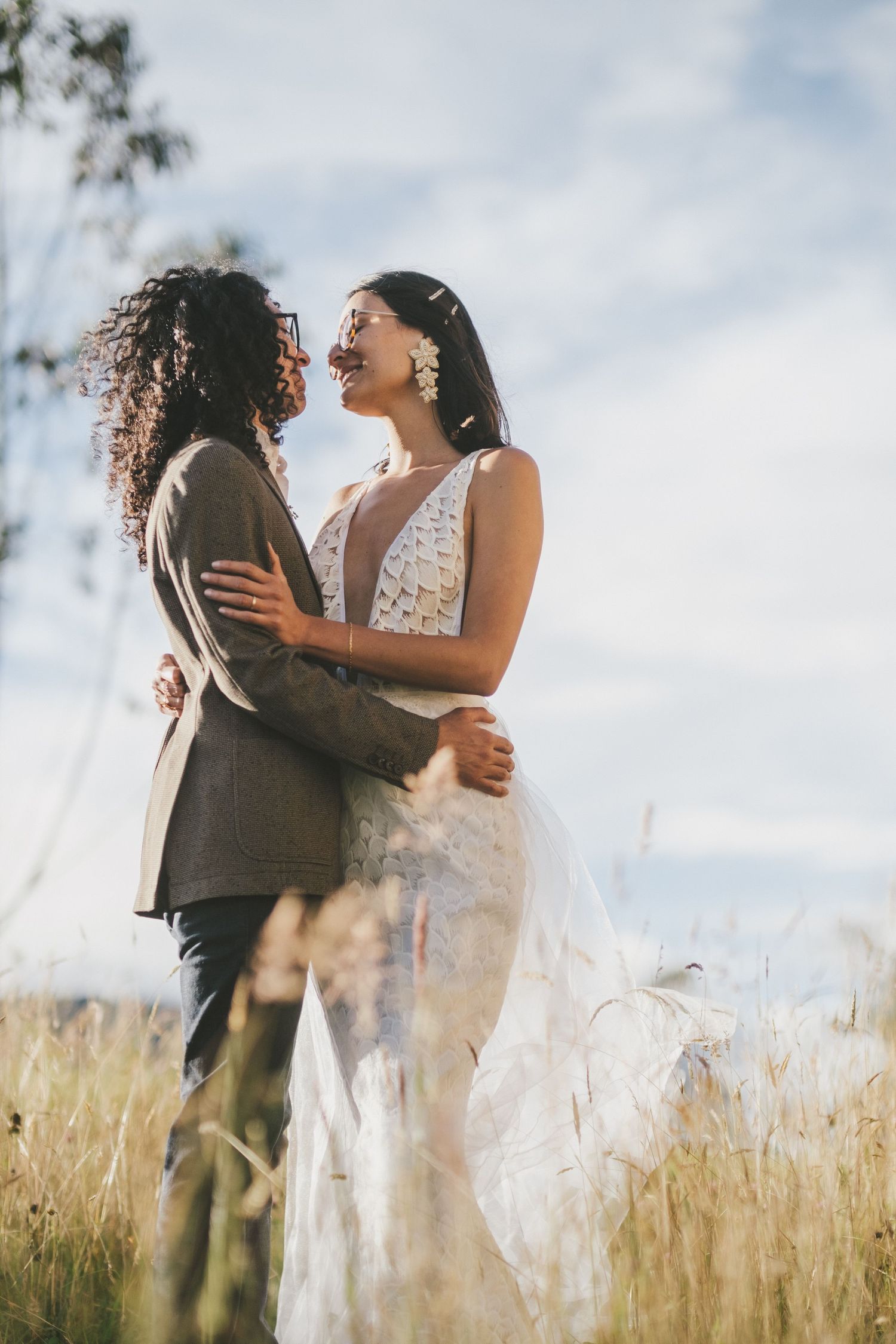 A romantic wedding couple embraces in a sun-lit meadow of tall grass during their outdoor photo session.