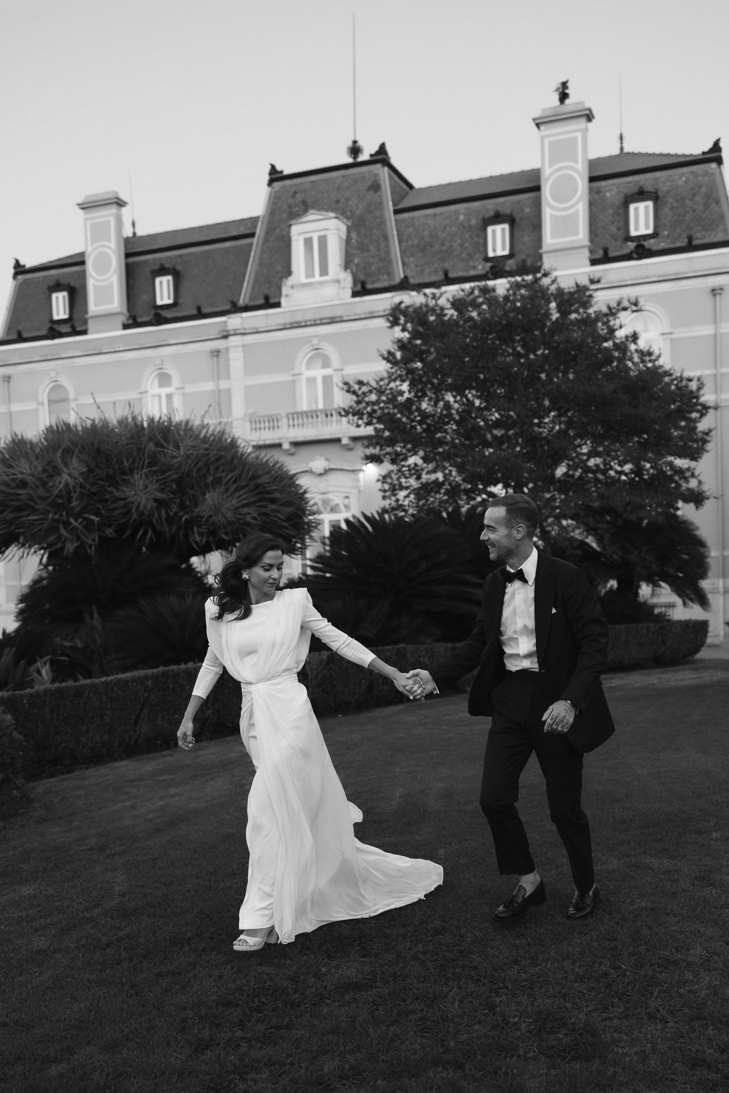 Joyful couple walking together at outdoor wedding celebration while guests cheer and throw confetti.