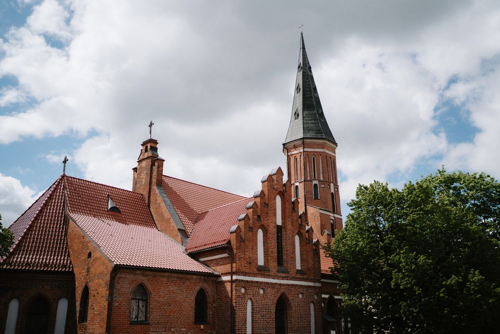 Red brick church with tall spires under dramatic cloudy sky.