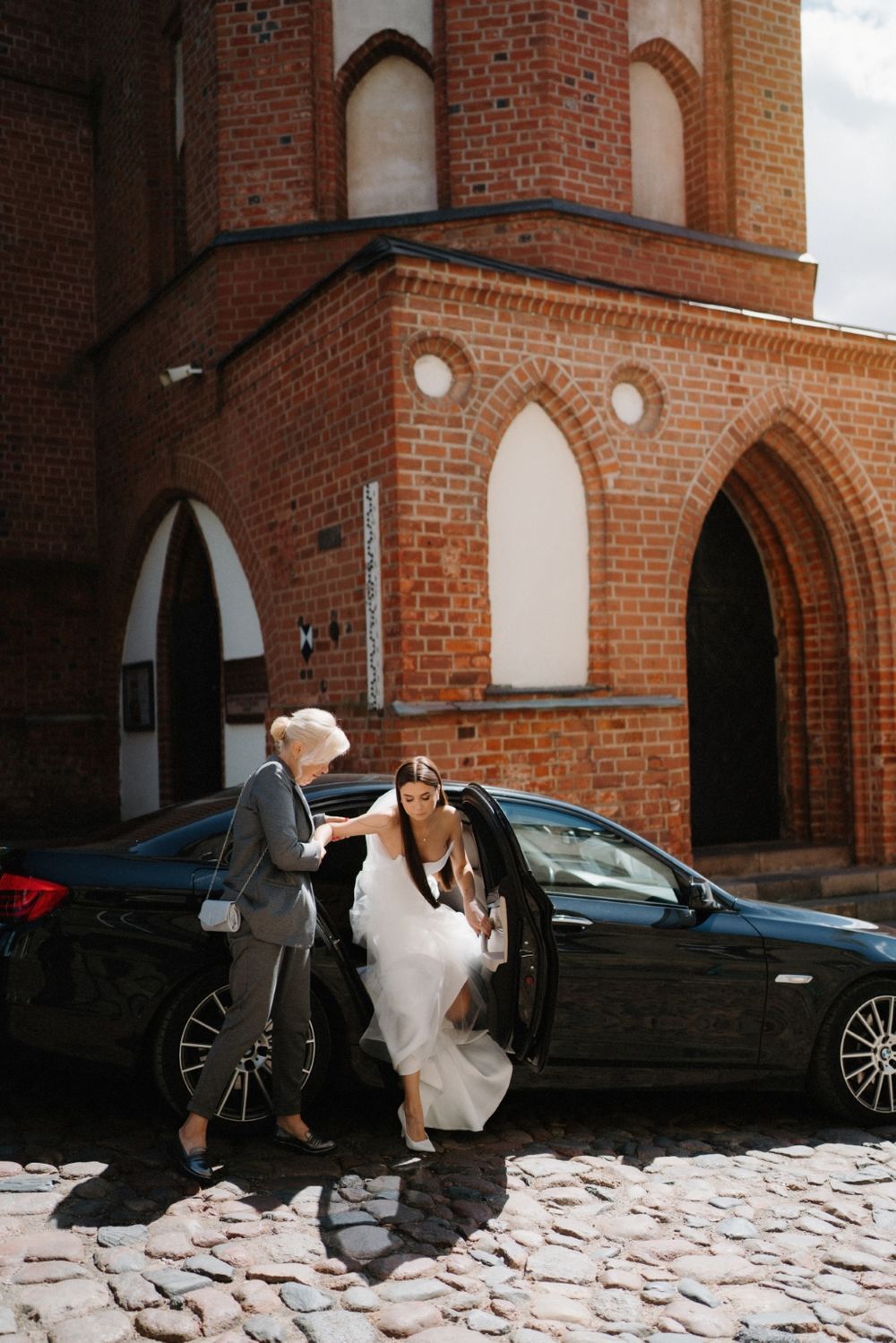 Wedding party poses near a black car outside a historic brick church.