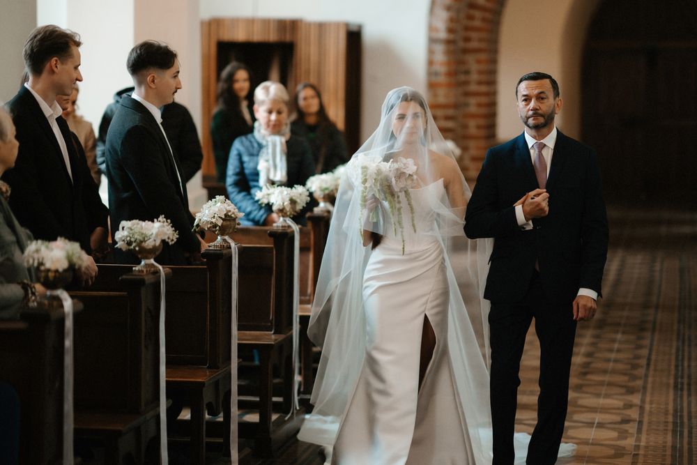 A wedding ceremony takes place in a beautiful brick church with elegant chandeliers and arched architecture.