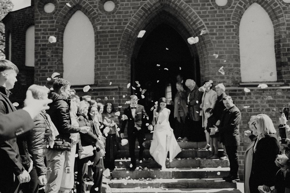 Black and white photo of wedding guests throwing confetti outside a brick church.