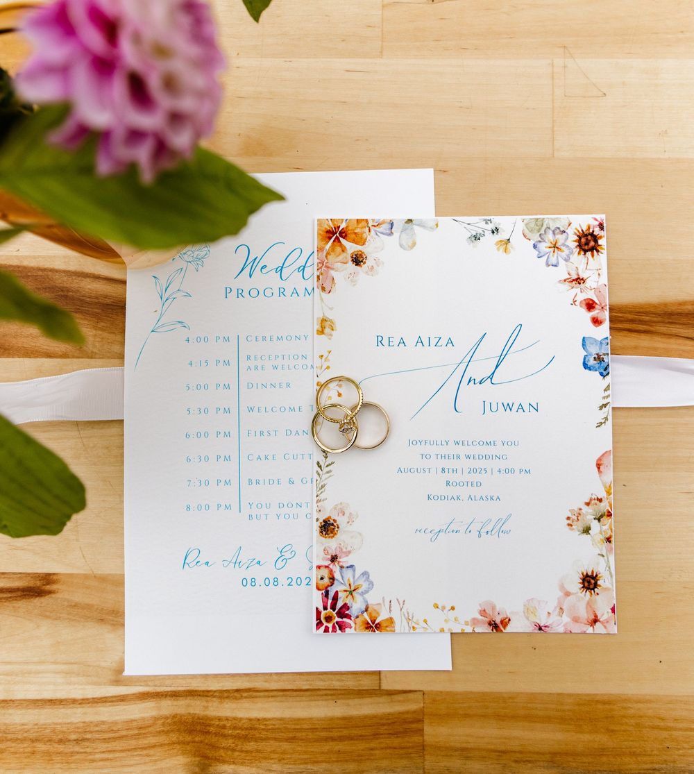 Wedding invitation cards with delicate floral details and elegant blue calligraphy displayed with wedding rings.
