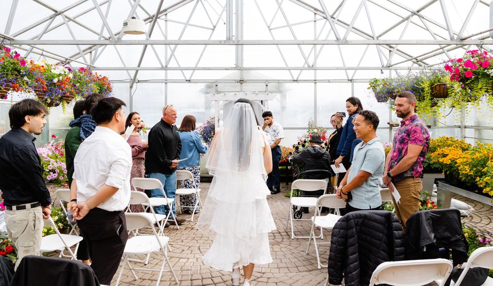A wedding celebration in a greenhouse conservatory decorated with colorful hanging floral arrangements.